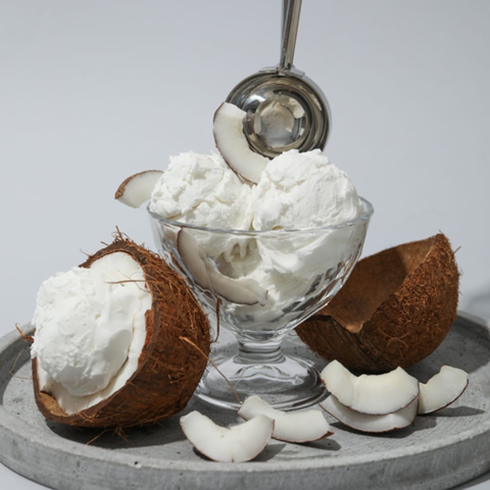 Coconut ice cream in a glass dish with a scoop, surrounded by coconut halves and flakes.