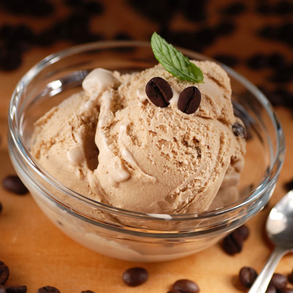 Coffee ice cream in a clear bowl, garnished with coffee beans and a mint leaf.