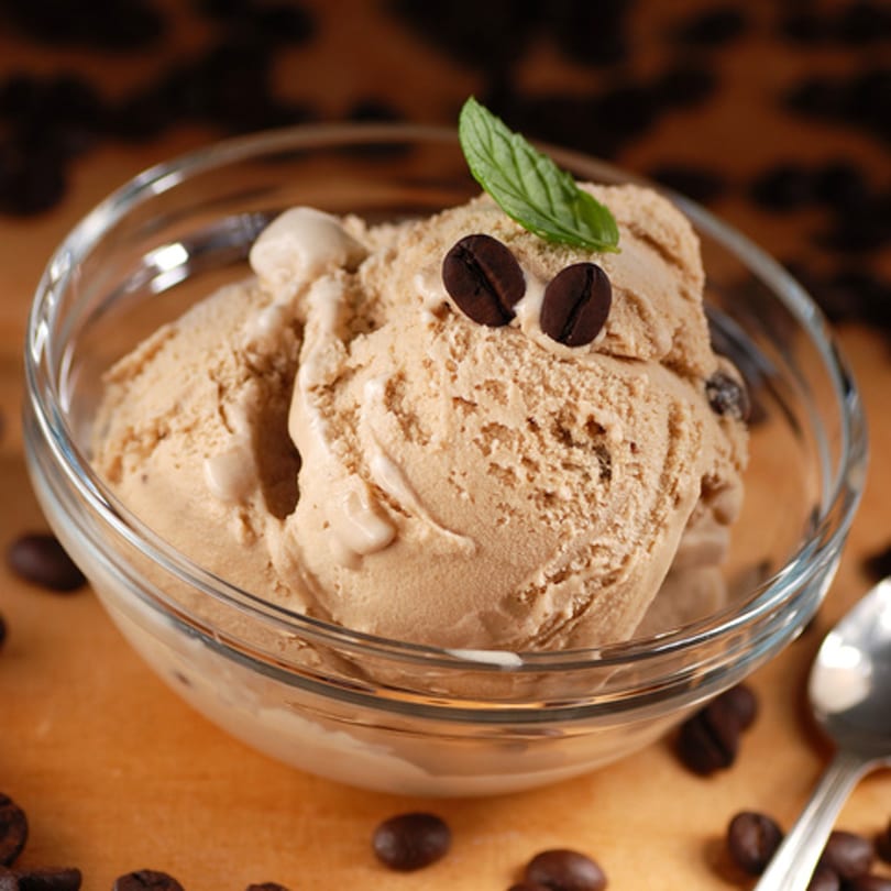 Coffee ice cream in a clear bowl, garnished with coffee beans and a mint leaf.