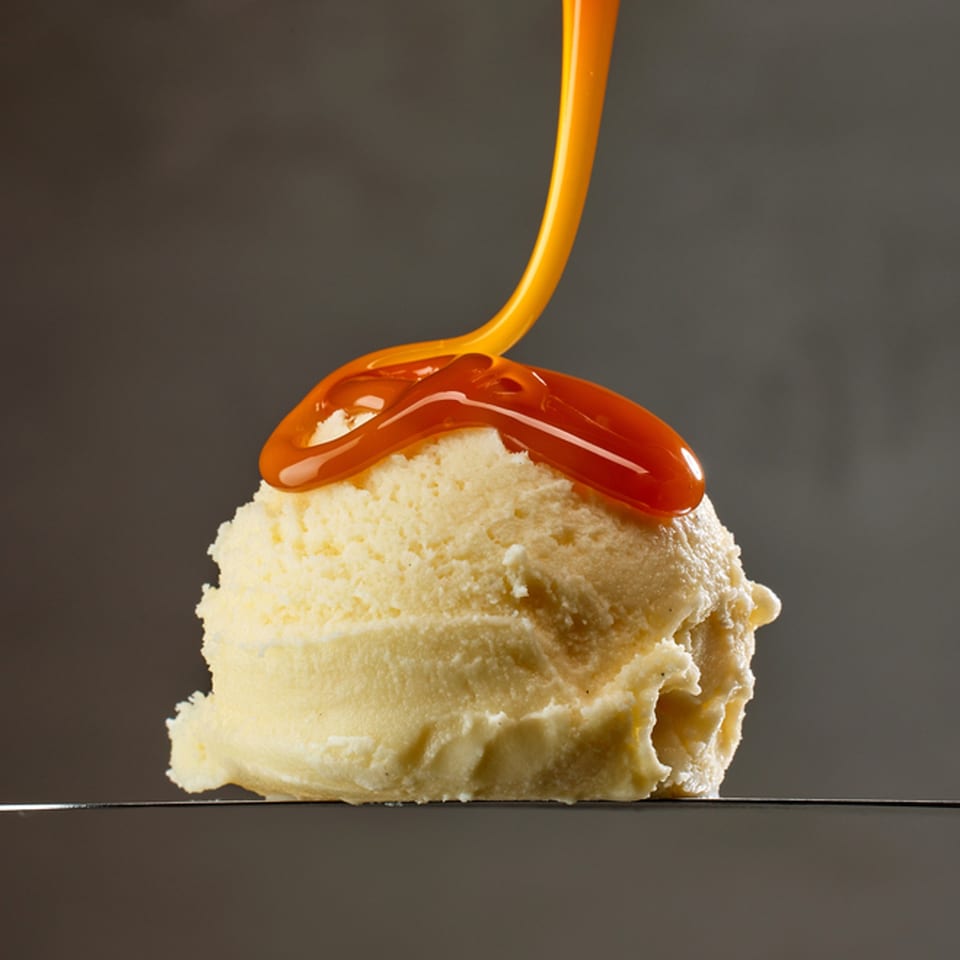 A scoop of vanilla ice cream with caramel sauce being poured over it.