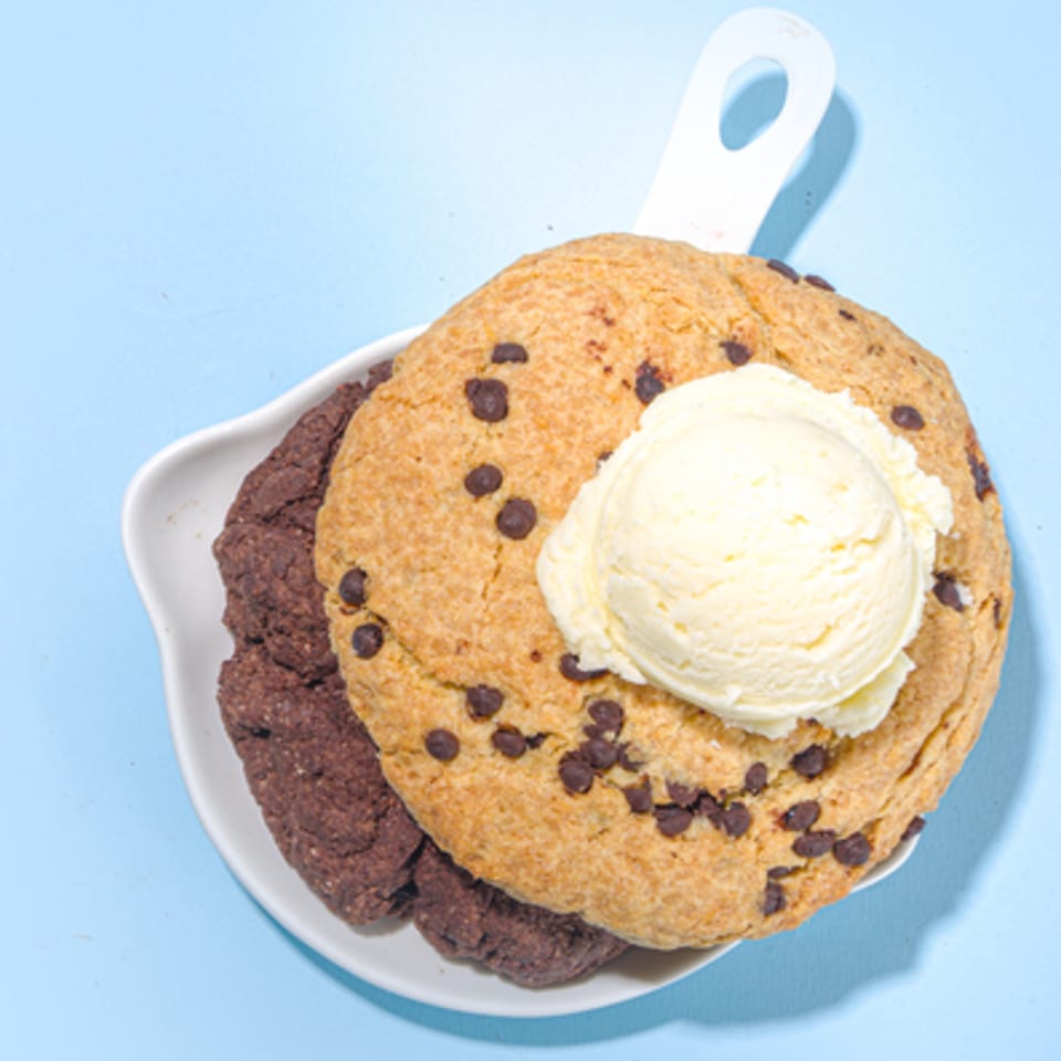 Two large cookies, one chocolate chip and one double chocolate, topped with a scoop of vanilla ice cream.